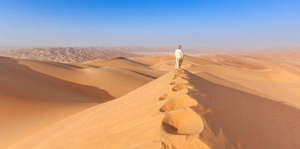 在当地 kandoura 装备走过一个沙丘在阿拉伯沙漠的阿布扎比阿拉伯男人