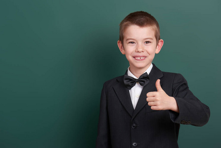 学校男孩显示最好的姿态，画像附近绿色空白黑板背景，身着经典的黑色西装，一名学生，教育理念