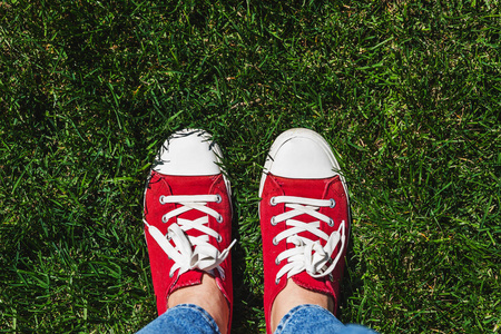 在旧的红色运动鞋，在绿色草地上的双腿。查看从上面。Co