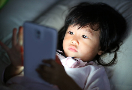 孩子玩智能手机在晚上躺在床上的女孩