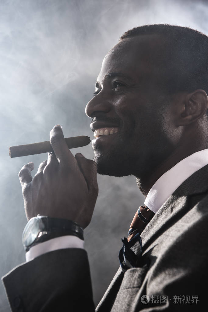 微笑充满自信的人吸烟雪茄在室内的侧面图