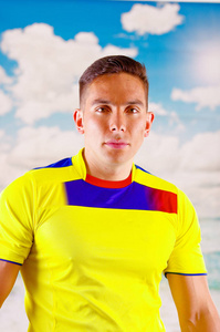 厄瓜多尔年轻人穿着正式马拉松足球衬衫站面对镜头，具有极大的热情，蓝蓝的天空和云背景非常有参与的肢体语言看比赛