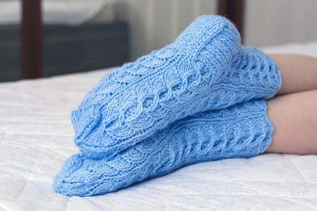 女性双腿下蓝色的羊毛袜子在床上的毯子。寒冷的天气，放松，在家休息