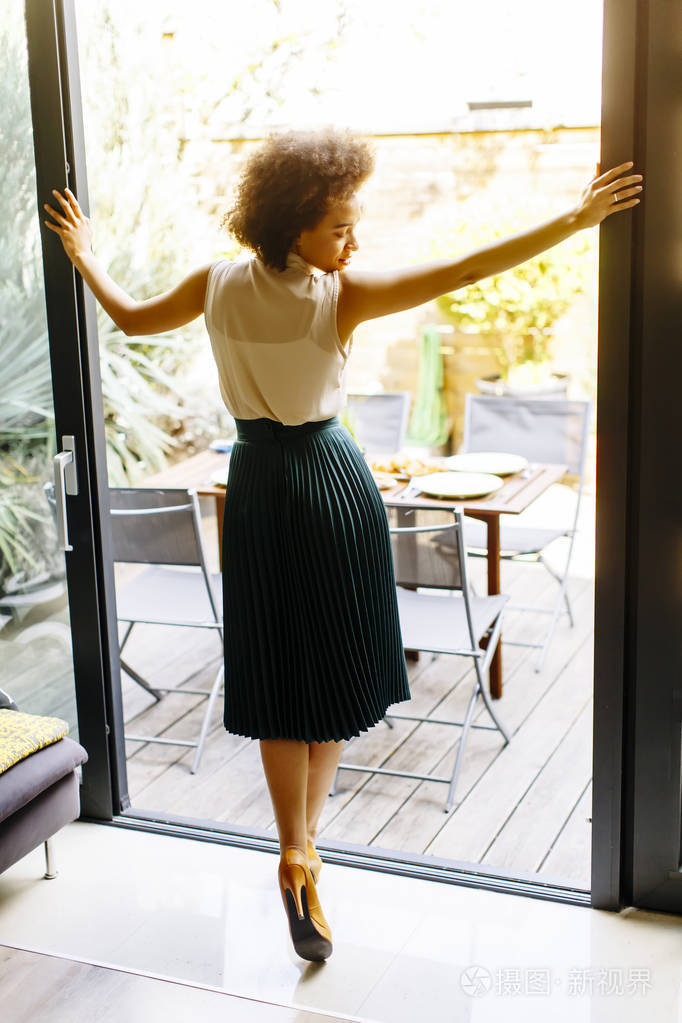 一位留着卷发的年轻女子在一扇敞开的玻璃门旁边的房子里