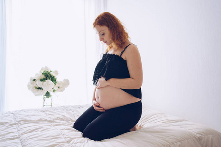 怀孕的女人坐在床上，摸她的肚子，用手