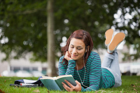 微笑的休闲学生躺在草地上看书