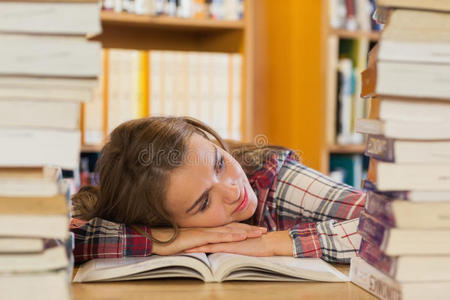 疲惫的漂亮学生头枕在书堆中间的桌子上