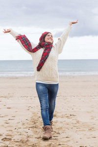 穿着暖和衣服的女人在海滩上伸展双臂