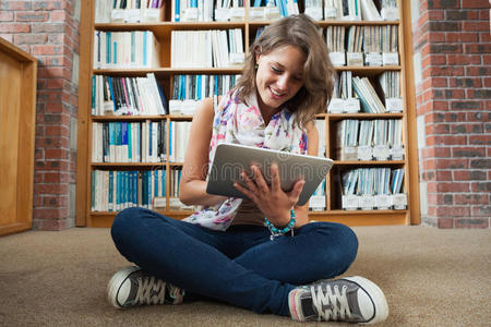 女学生在图书馆地板上用平板电脑对着书架