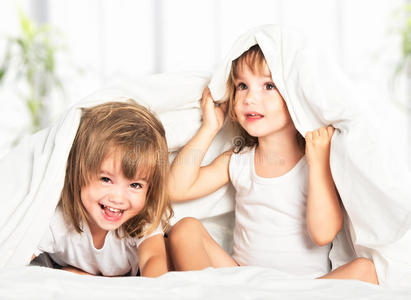 快乐的小女孩双胞胎妹妹在床上的毯子下