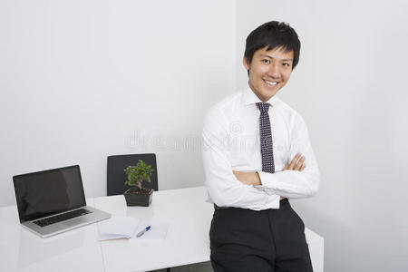 办公桌上双臂交叉的快乐亚洲商人画像