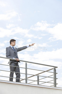 年轻的商人举着胳膊站在露台的栏杆上，对着天空