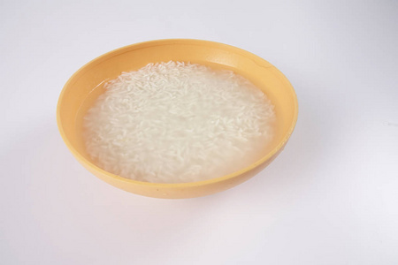 将米浸泡在白色背景的黄色碗中图片