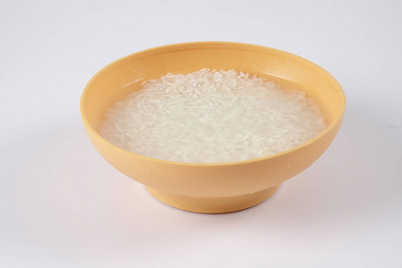 将米浸泡在白色背景的黄色碗中图片