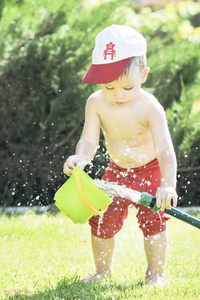 小男孩倒在花园里的软管从在炎热的夏天，绿色的草坪上，泼水