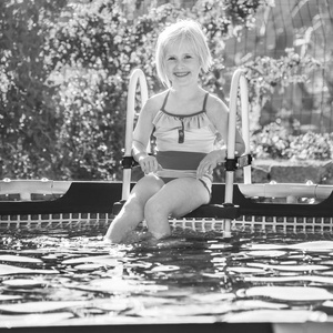 有趣的周末露天矿。 微笑健康的女孩穿着五颜六色的泳衣坐在游泳池里