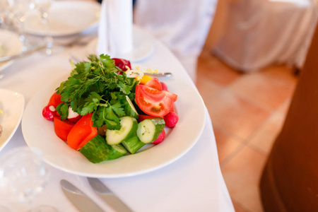 美味的夏季沙拉, 桌上的白色盘子上有新鲜的蔬菜。黄瓜西红柿萝卜和生菜