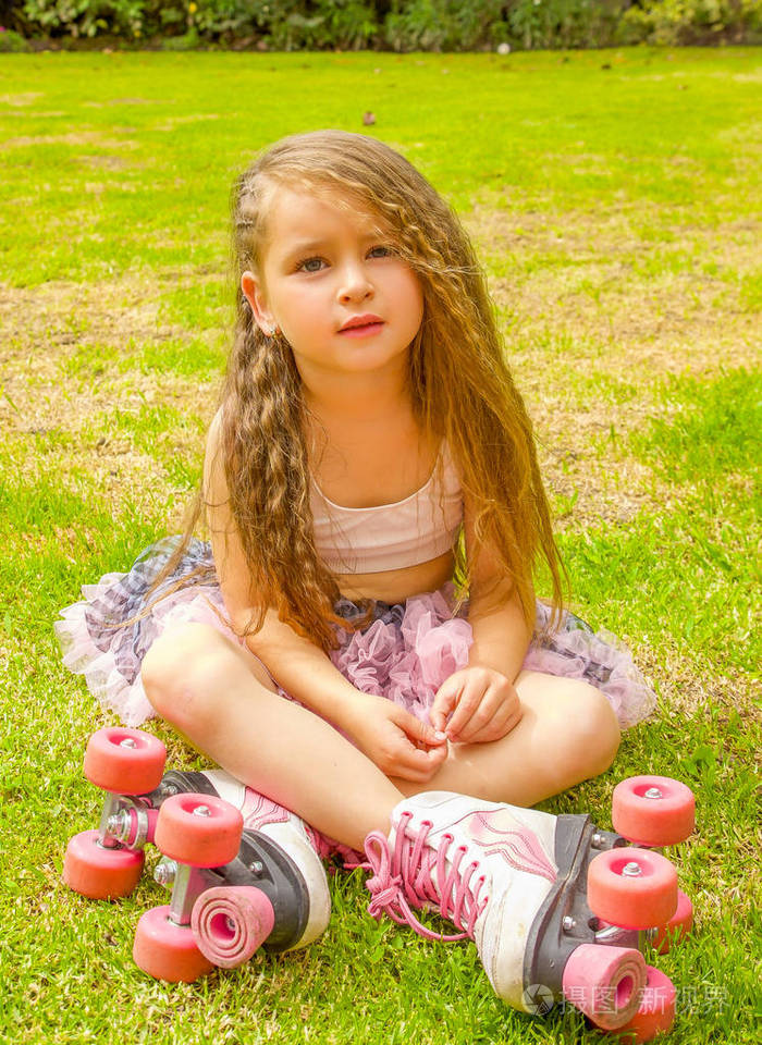 小女孩幼儿园坐在后院, 穿着溜冰鞋, 交叉双腿, 在花园的背景下照片