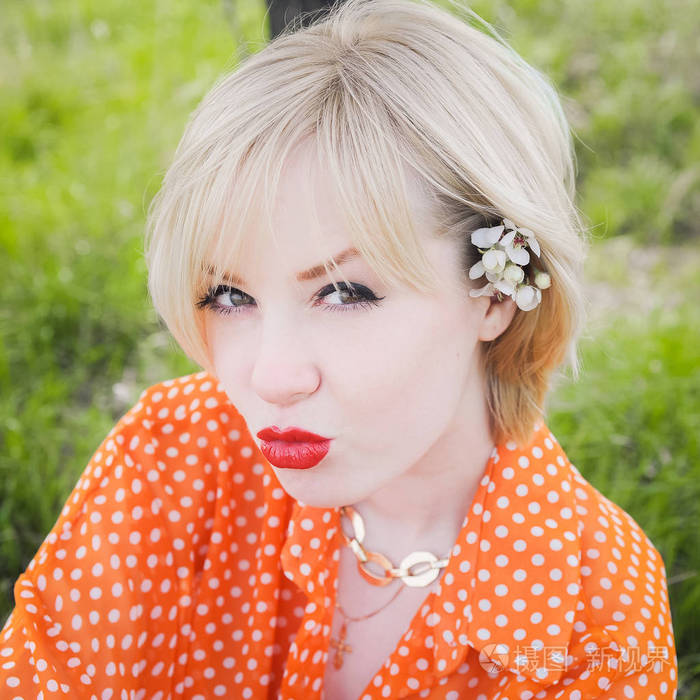 肖像户外年轻漂亮的女孩在橙色时髦金发明亮开朗圆点毛衫，微笑红丰满圆润的嘴唇上的绿草背景