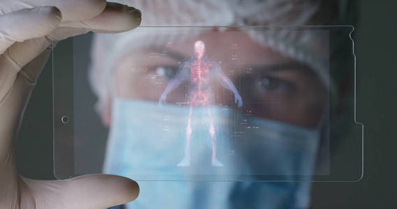 未来的医生，一名外科医生，看着技术数字全息显示器，人类的全息图，医用口罩，蓝色的长袍。概念未来派医学 医生 实验室 未来