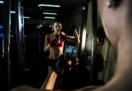 年轻成年女性的肖像与智能手机自拍在健身房。 体育健身生活方式技术与人的观念