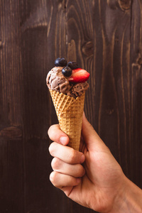 手里拿着巧克力冰激淋与浆果的木制的背景