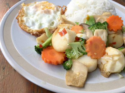 在木制背景下，将炒菜豆腐与米饭和煎蛋混合在白色盘子中。素食，健康食品..