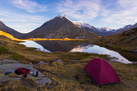 带上阿尔卑斯山的高原湖附近的帐篷露营。白雪皑皑的山脉和景区色彩斑斓的天空在日落时的反射。冒险与探索