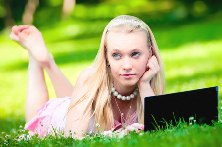 美丽的金发女郎与笔记本电脑的草地上