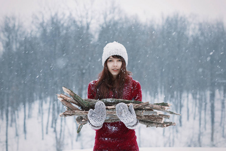 美丽的冰冻的女孩坚持冬天雪林走过来燃烧的木头。与 mittend 和木柴的女孩。温暖，在雪寒冷的冬天来燃烧的木头。抱着柴火