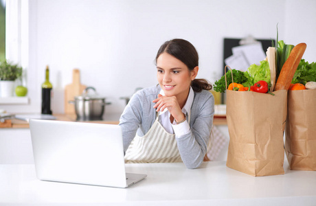 面带笑容的女人，网上购物在厨房中使用计算机和信用卡