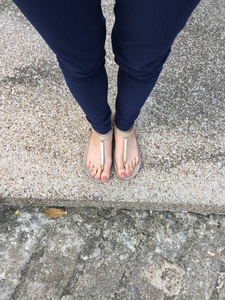 特写脚与棕色钉子在黄金凉鞋和蓝色裤子在女性脚在地面背景