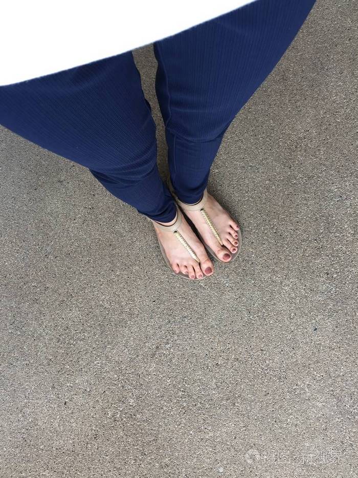 特写脚与棕色钉子在黄金凉鞋和蓝色裤子在女性脚在地面背景照片-正版