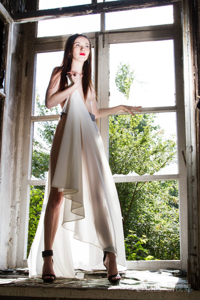 赤裸乳房的女孩站在一所废弃的房子的窗户开口里
