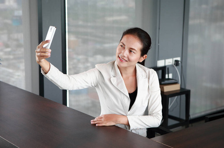 微笑女商人持有智能手机在工作场所使用的智能手机,拍照的自己的办公