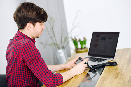 年轻和成功的人使用无反光镜相机和坐在一张桌子在办公室的一台笔记本电脑