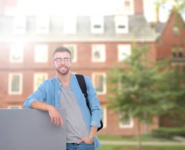 一个微笑的男学生，持有空白板站在大街上的肖像