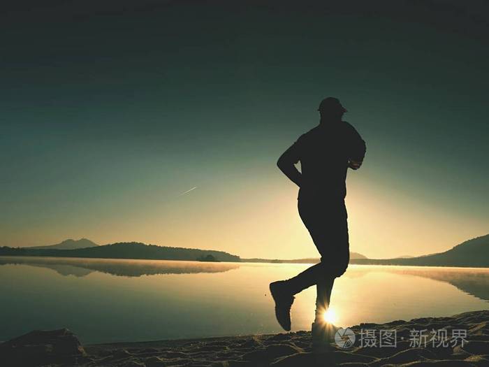 人行使和日出时在湖滩上伸展健康的生活方式孤独的年轻健身人行使在