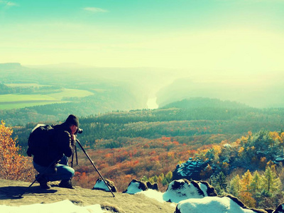 悬崖上的专业。自然摄影师带镜相机在白雪皑皑的岩石上的照片