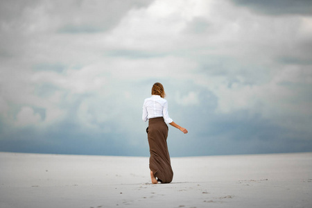 年轻女子赤脚在沙漠里.后视图照片