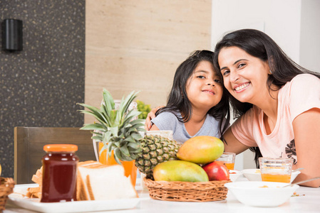 一个有吸引力快乐 微笑着亚洲印度家庭的母亲和女儿在一张餐桌吃健康的食物与沙拉。印度人吃早餐 午餐或晚餐。选择性的焦点