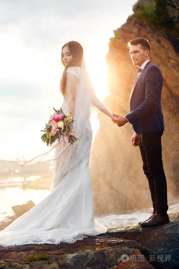 美丽的夫妇在爱接吻时站在海边的岩石上.