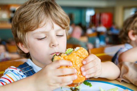 可爱健康学龄前孩子吃汉堡包坐在学校的食堂