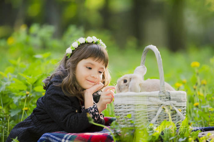 一个小女孩在一个花圈观察在篮子里的一只兔子在日落时在一个公园里
