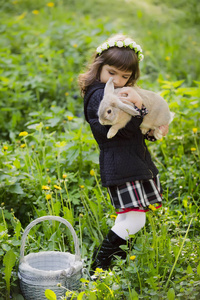 一个小女孩在一个花圈观察在篮子里的一只兔子在日落时在一个公园里