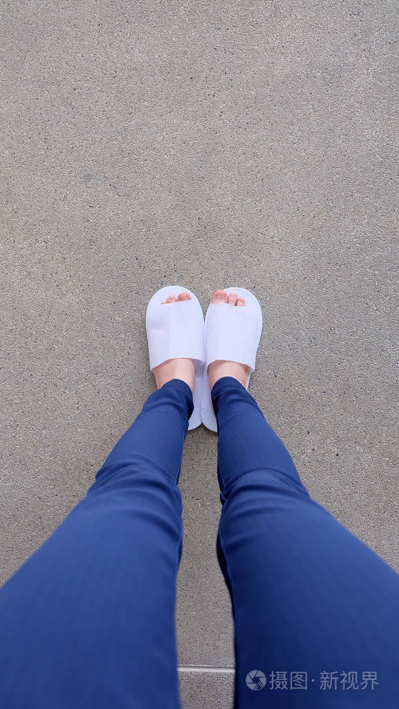 年轻女性的腿和脚上还穿着白色的拖鞋和蓝色裤子上地面室内背景