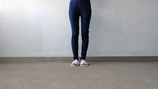 年轻女性的腿和脚上还穿着白色的拖鞋和蓝色裤子上地面,室内背景照片