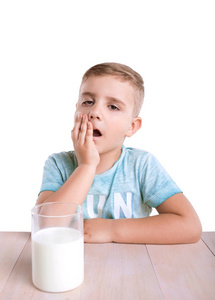 可爱的孩子在一个蓝色的 t 恤坐和靠近他，充满了美味的牛奶，在他身边，木制的桌子上的玻璃隔离在白色背景上