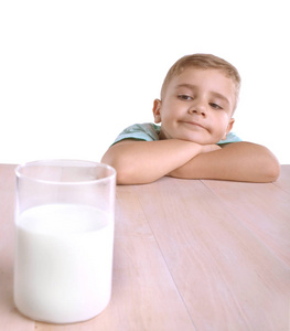 可爱白种人的孩子，一头金发，蓝色 t 恤与巨大的玻璃充满营养可口的牛奶，在褐色的木桌，一个白色的背景上孤立
