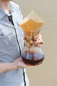选择的咖啡酿造在沙滩背景的年轻人手中的手